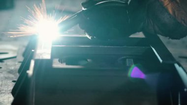 Meşale endüstriyel bir tezgahta çeliği kaynatırken parlak kıvılcımlar uçuşan kaynak yapan bir işçinin yakın çekimi. Yavaş çekim.