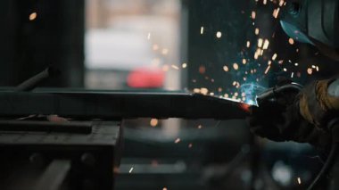 Koruyucu giysiler içindeki kaynakçı atölyedeki metal parçaları kaynaklıyor. Yavaş çekim.