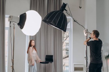 Bir fotoğrafçı stüdyodaki ışıklandırmayı genç bir kızıl saçlının portresini çekmek için ayarlıyor..