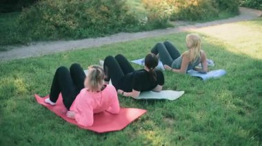 Yeşil bir parkta yoga minderleri üzerinde egzersiz yapan bir grup kadın, dışarıda spor yapıyor ve sağlıklı yaşam tarzına, sağlığına ve aktif yaşama odaklanıyor..