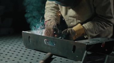 Koruyucu giysiler içindeki kaynakçı atölyedeki metal parçaları kaynaklıyor. Yavaş çekim.