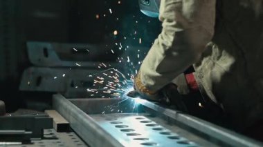 Koruyucu giysiler içindeki kaynakçı atölyedeki metal parçaları kaynaklıyor. Yavaş çekim.