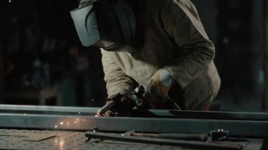 Koruyucu giysiler içindeki kaynakçı atölyedeki metal parçaları kaynaklıyor. Yavaş çekim.