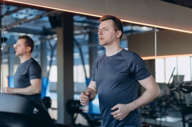 Modern spor salonunda koşu bandına odaklanmış yetişkin bir adam ayna yansıması ve sıcak ışıklandırma ile, dayanıklılık, zindelik ve genel sağlık düzeyini iyileştirmek için kardiyo çalışması yapıyor..