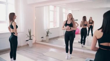 Beden eğitiminde grup çalışması. Bir grup genç zayıf kadın ısınma turu yapıyor. Antrenör egzersizleri gösterir..