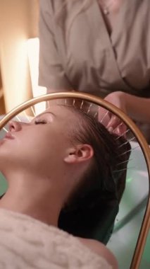 Genç bir kadın Japon baş masajı sırasında özel bir saç yıkama aletinden akan su ile kaplıca tedavisi görüyor..