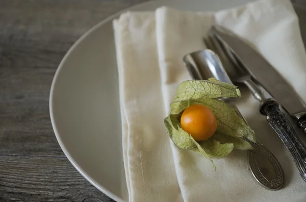 Vintage bestek en servies op oude houten tafel, landelijke stijl in laag natuurlijk licht met een oranje alkekengi — Stockfoto