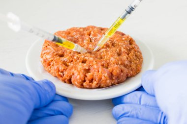 Antibiyotiklerle dolu çiğ sığır burger. Ete saplanmış şırıngalar, konsept, sağlıksız yiyecekler