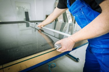 Camcının çalışanı camı özel bir aletle kesiyor. Cam Fabrikası