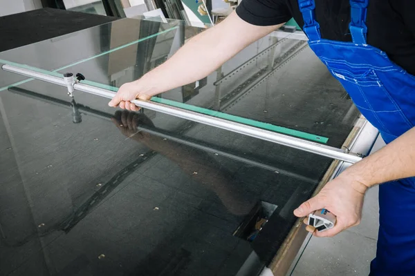 玻璃窗工在工作场所的专业桌子上用刀片把玻璃割破 — 图库照片
