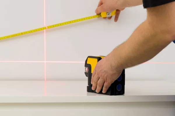 the specialist uses an electronic laser to check right angles and lines while taking measurements of the room