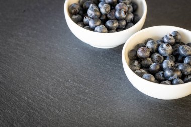 Taze ve sağlıklı yaban mersinleri kaselerde taş tezgahın üzerinde duruyor. Kendi yazıtın için yer 