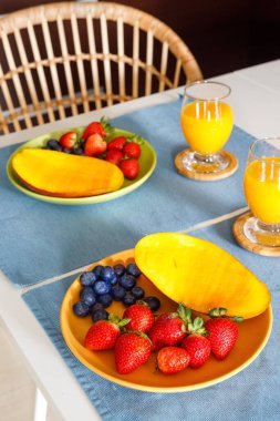 Sağlıklı bir yemek, iki tabak taze çilek, mango ve yaban mersini, ve mutfak masasında portakal suyu. iyi kaloriler, düzgün beslenme, meyve yeme, dikey fotoğraf 