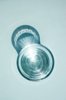 A glass of clear water, Minimal layout, Light reflection, Shadow play. Pastel blue background