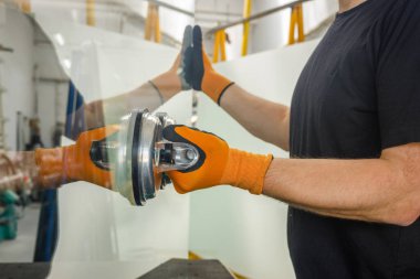 Glazier pencereler için bir enayi kullanıyor. Cam yapım atölyesi, adam özel aletlerin yardımıyla masanın üzerindeki kalın cam levhayı kaldırır.