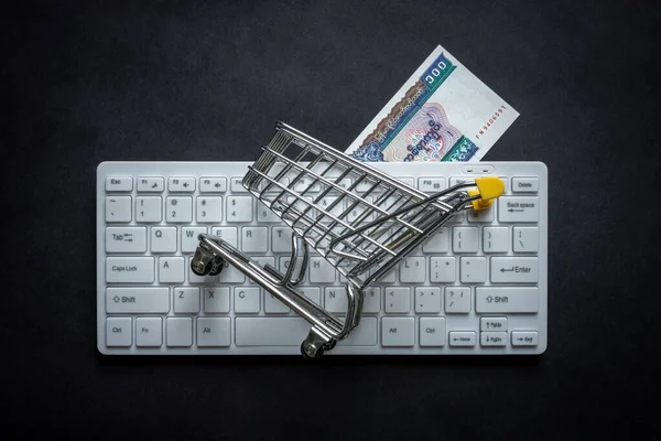 Myanmar money, White computer keyboard, Miniature shopping cart, Black background, Online shopping concept in stores, Low prices