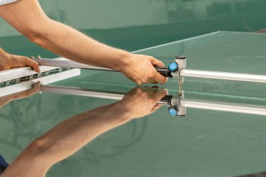 Cam fabrikasındaki bir çalışan özel ekipmanlarla cam kesiyor. 
