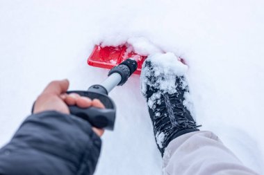 Winter, kar küreyen bir adam, yakın plan, kırmızı bir kar küreğiyle. Şiddetli kar yağışı, soğuk ve negatif sıcaklık