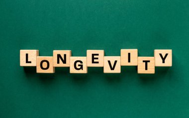 Uzun ömürlülük kelimesi tahta bloklara yazıldı. Uzun ömürlü olma kavramı. Yemek alışkanlıkları, olumlu tavırlar, sosyal ilişkiler ve fiziksel aktivite. Güzel koyu yeşil arka plan. Düz yatıyordu. Boşluğu kopyala