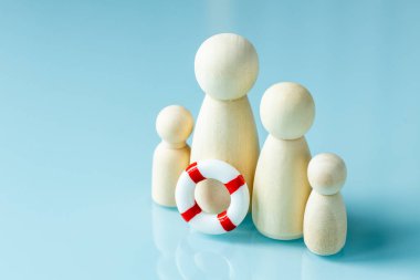 Ailelere yardım. Sosyal konsept. Tahta heykelcikler çocuklu bir aileyi ve bir hayat kurtarıcıyı simgeliyor. Büyük aileler için yardım programları ve hükümet desteği