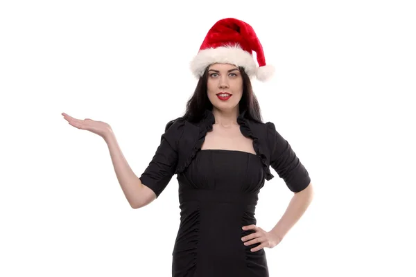 Портрет молодого взрослого красивого стройная брюнетка женщина в черном платье и красный Санта-Клаус шляпу помощника показывая что-то изолированное на белом фоне — стоковое фото
