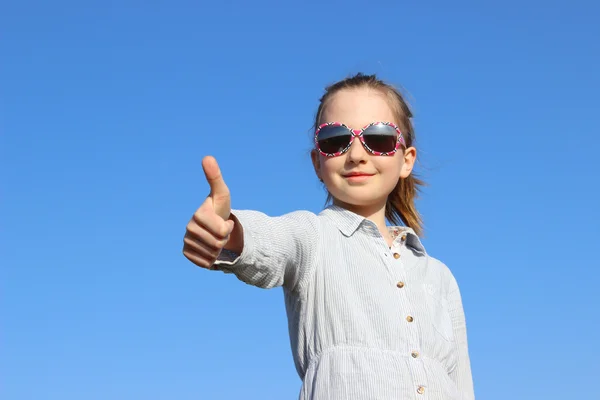 Portret dziewczynki sobie na okulary i białej koszuli kciuki skrzyżowane się na tle niebieskiego nieba — Zdjęcie stockowe