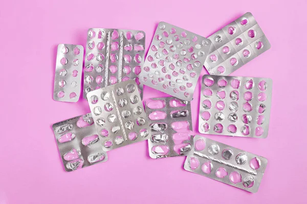 empty blister packs of pills with one partially full pack on pink background. flat lay simple composition, top view.