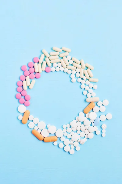 creative medicine compositions. the frame of tablets and capsules, different shapes on a light blue background. vitamins for skin, hair, and nails. flat lay, vertical frame.