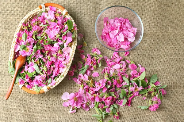 fragrant rose petals and flowers scattered on the background of canvas fabric. a glass bowl and a wicker basket with pink flowers. top view, flat lay.