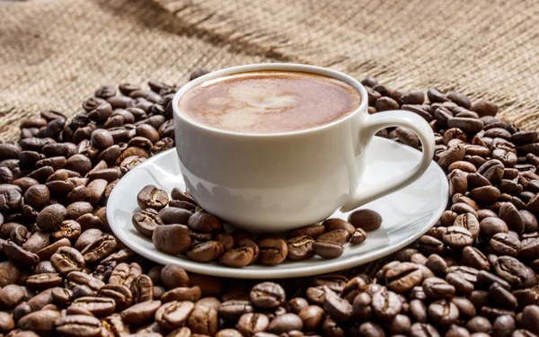 Grains de café sur une planche de bois et une tasse de café — Photo