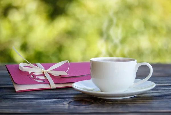 Taza de café y un sobre sobre sobre una mesa de madera — Foto de Stock