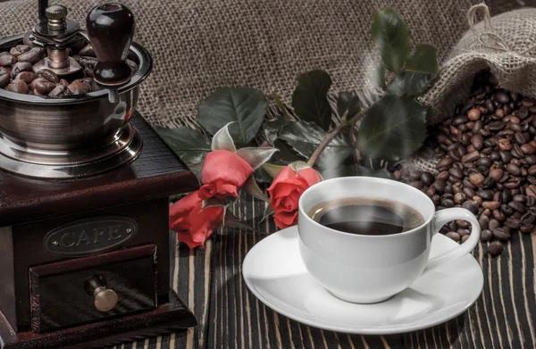 Molinillo de café, rosa roja y taza de café en escritorio de madera —  Fotos de Stock
