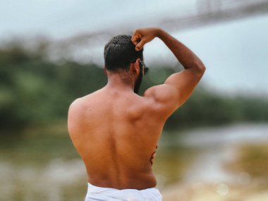 Göz kamaştırıcı kas yapısını ve Hint vücut geliştiricisinin sırtının tanımını göstermek için dikiz aynasından çekilmiş doğal, engebeli bir dış görünüme karşı..