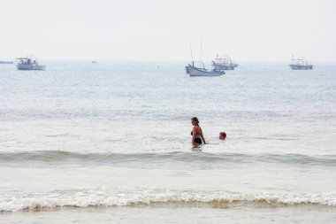 6 Aralık 2025, Panaji, Goa, Hindistan, Goa 'daki Baga Sahili' nde canlı bir sahne insanların yüzüşünü ve canlı kıyı şeridi boyunca demirleyen tekneleri gösteriyor..