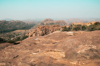 Geniş açılı fotoğraf, Hampi 'nin taşra yerleşimleriyle çevrili dramatik kaya parçalı manzarasını yakalar. Sahne tarihi seyahat yerleri, arkeolojik bölgeler ve sakin Güney Hindistan manzaralarını temsil ediyor..