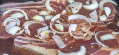 Çiğ biftek, pirzola dilimlenmiş soğan ve kırmızı biber taneleriyle marine ediliyor.