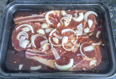 Çiğ biftek, pirzola dilimlenmiş soğan ve kırmızı biber taneleriyle marine ediliyor.