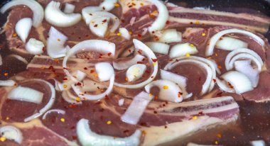 Çiğ biftek, pirzola dilimlenmiş soğan ve kırmızı biber taneleriyle marine ediliyor.