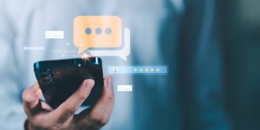 Parlak geri bildirim ve beş yıldızlı derecelendirme simgelerine sahip akıllı telefon tutan kişi, çevrimiçi değerlendirmeyi, müşteri memnuniyetini, dijital iletişimi ve mobil geri bildirim teknolojisi kavramını temsil ediyor.