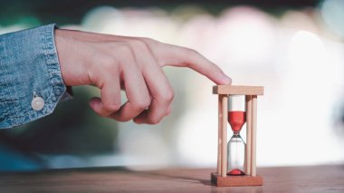 Bir el kırmızı kumla ahşap bir kum saatine dokunuyor, 2026 hedefe giden zamanı sembolize ediyor, teslim tarihini, sabrı, zaman yönetimini ve gelecekteki başarının aciliyetini temsil ediyor..