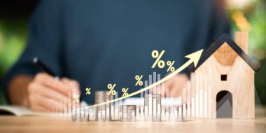 İstiflenmiş madeni paralar, yüzdelik semboller, ahşap evin yanında yükselen ok, yükselen mortgage oranlarını, emlak değeri artışını, konut finans analizini sembolize eden emlak yatırım büyümesi konsepti