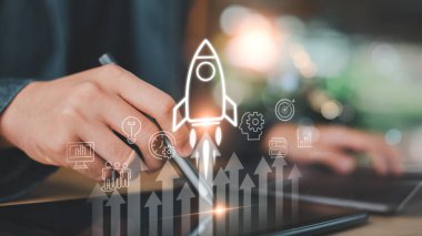 Roket fırlatma sembolü, kar büyüme okları, yenilik simgeleri, stratejik planlama ve ölçeklenebilir başarı için piyasa geliştirme analizleri ile tablet üzerindeki dijital performansı izleyen girişimci.