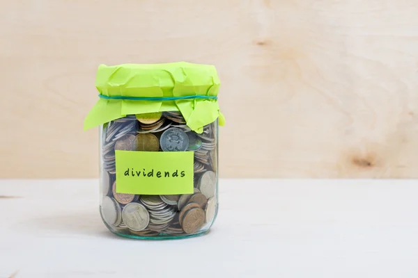 Financial concept. Coins in glass money jar with dividends label. Wooden background — Stock Photo, Image