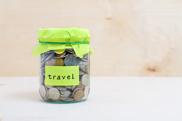 Finanční koncept. Mince v peníze sklenice s popiskem cestování. Dřevěné pozadí — Stock fotografie