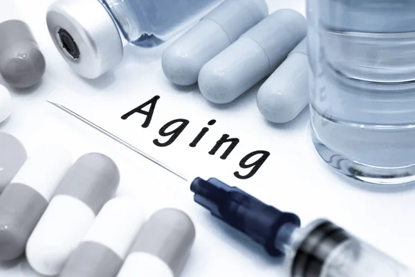 Aging - diagnosis written on a white piece of paper. Syringe and vaccine with drugs — Stock Photo, Image