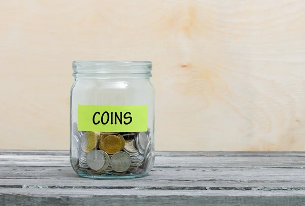 Label on a glass jar with the inscription - coins. Glass jar with coins. Financial concept on wooden background — Stock Photo, Image