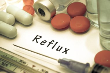 Reflux- diagnosis written on a white piece of paper. Syringe and vaccine with drugs. clipart