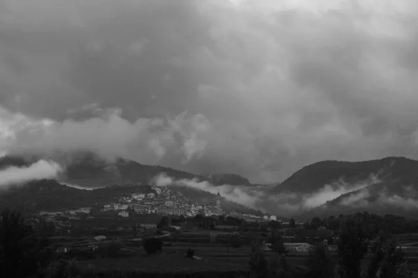 Dağlarla çevrili bir vadide beliren Penyarroya köyü ve siyah beyaz bir manzarada bulutlu, karamsar bir gökyüzü.