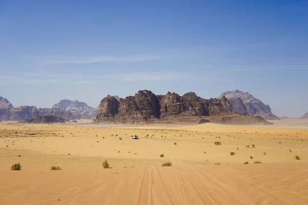 White 4x4 vehicle driving through the vast desert landscape of Wadi Rum, Jordan, exploring the rugged mountains and sand