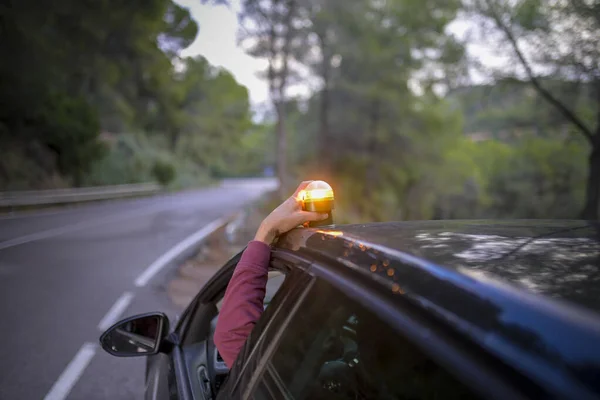 Person placing a V16 emergency beacon onto the car roof on a roadside at dusk, indicating a breakdown for safety